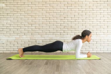 Latin kadın beyaz tuğlalı minder üzerinde yoga yapıyor.