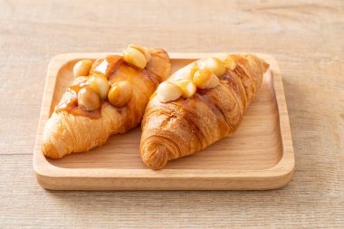 Macadamia ve ahşap tabakta karamel ile kruvasan.