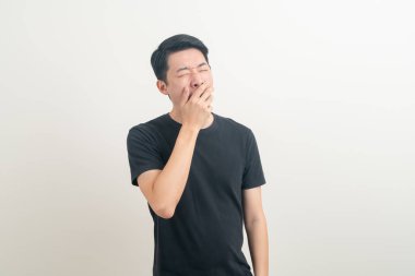 Esnemiş suratlı ve beyaz arka planda uykulu genç bir Asyalı.