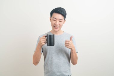 Genç Asyalı adam elinde kahve fincanı beyaz arka planda gülümseyen yüzüyle