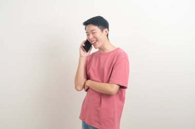 Genç Asyalı adam beyaz arka planda mutlu yüzlü akıllı telefon ve cep telefonu kullanıyor veya konuşuyor