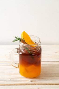 Bir bardak buzlu americano sade kahve ve ahşap arka planda biberiye ve tarçınla süslenmiş portakal ve limon suyu.