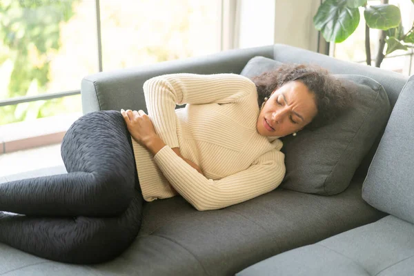 ラテン女性横たわっソファに自宅で腹痛感 — ストック写真