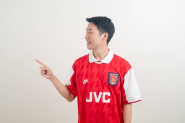 Bangkok, THAILAND - 27 Kasım 2021: beyaz arka planda Arsenal tişörtü giyen genç Asyalı. Arsenal, Londra 'nın en ünlü futbol kulübüdür..