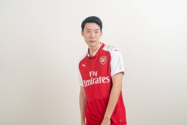 Bangkok, THAILAND - 27 Kasım 2021: beyaz arka planda Arsenal tişörtü giyen genç Asyalı. Arsenal, Londra 'nın en ünlü futbol kulübüdür..