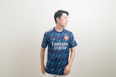 Bangkok, THAILAND - 27 Kasım 2021: beyaz arka planda Arsenal tişörtü giyen genç Asyalı. Arsenal, Londra 'nın en ünlü futbol kulübüdür..