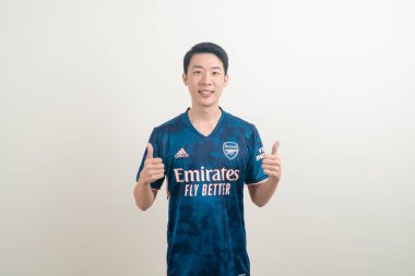 Bangkok, THAILAND - 27 Kasım 2021: beyaz arka planda Arsenal tişörtü giyen genç Asyalı. Arsenal, Londra 'nın en ünlü futbol kulübüdür..