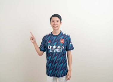 Bangkok, THAILAND - 27 Kasım 2021: beyaz arka planda Arsenal tişörtü giyen genç Asyalı. Arsenal, Londra 'nın en ünlü futbol kulübüdür..