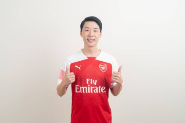 Bangkok, THAILAND - 27 Kasım 2021: beyaz arka planda Arsenal tişörtü giyen genç Asyalı. Arsenal, Londra 'nın en ünlü futbol kulübüdür..
