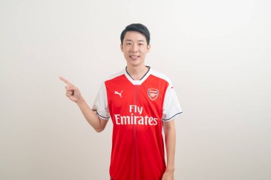 Bangkok, THAILAND - 27 Kasım 2021: beyaz arka planda Arsenal tişörtü giyen genç Asyalı. Arsenal, Londra 'nın en ünlü futbol kulübüdür..