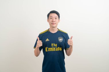 Bangkok, THAILAND - 27 Kasım 2021: beyaz arka planda Arsenal tişörtü giyen genç Asyalı. Arsenal, Londra 'nın en ünlü futbol kulübüdür..