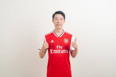 Bangkok, THAILAND - 27 Kasım 2021: beyaz arka planda Arsenal tişörtü giyen genç Asyalı. Arsenal, Londra 'nın en ünlü futbol kulübüdür..