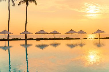 Günbatımında ya da gün doğumunda okyanus arka planında yüzme havuzunun etrafında yüzen şemsiyeli - tatil ve tatil kavramı