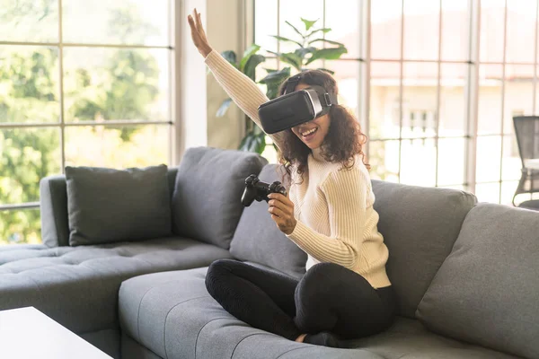 Latin bir kadın evdeki kanepede sanal gerçeklik kulaklığı kullanıyor.