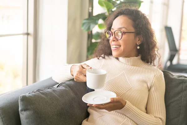 Latin bir kadın evdeki kanepede kahve içiyor. Eski moda efekt filtresi.