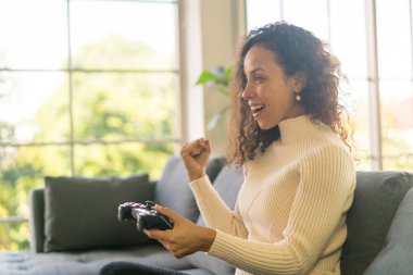 Laitin denen kadın evdeki kanepede elinde joystick ile video oyunları oynuyor.