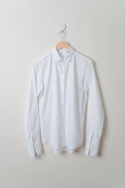 Duvarında ahşap askı olan beyaz gömlek asılı.