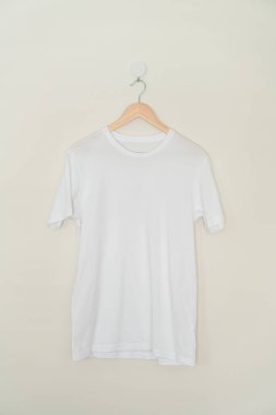 white t-shirt hanging with wood hanger on wall