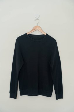 black sweater hanging with wood hanger on wall