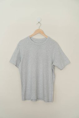 grey t-shirt hanging with wood hanger on wall