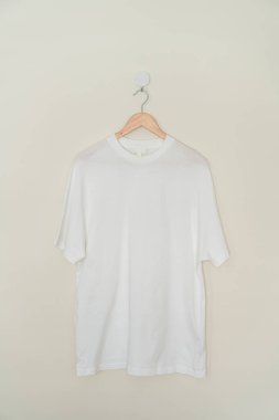 white t-shirt hanging with wood hanger on wall