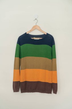 colorful sweater hanging with wood hanger on wall