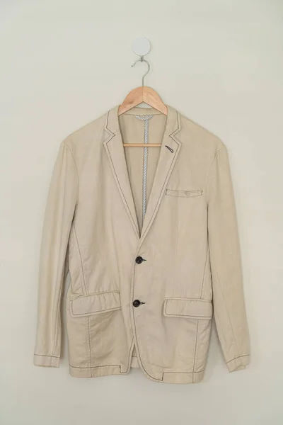 beige suit hanging with wood hanger on wall