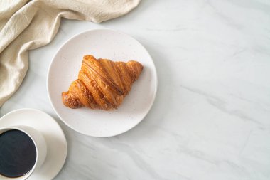 Beyaz tabakta taze kruvasan ve siyah kahve.