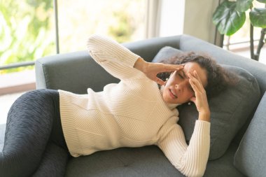 Latin kadın evdeki kanepede uzanmış baş ağrısı çekiyor.