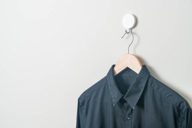 Duvarında ahşap askı olan siyah bir gömlek asıyor.