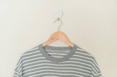 grey t-shirt hanging with wood hanger on wall