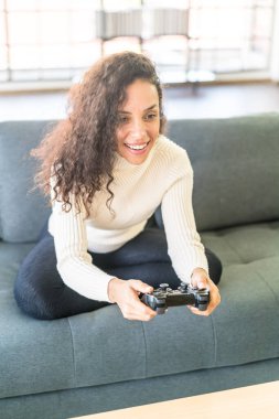 Laitin denen kadın evdeki kanepede elinde joystick ile video oyunları oynuyor.