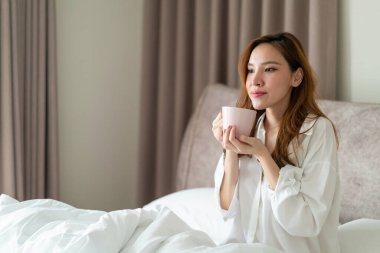 Portre güzel Asyalı kadın uyanır ve elinde kahve fincanı ya da kupayla sabah uyanır.