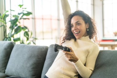 Laitin denen kadın evdeki kanepede elinde joystick ile video oyunları oynuyor.