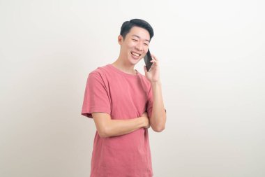 Genç Asyalı adam beyaz arka planda mutlu yüzlü akıllı telefon ve cep telefonu kullanıyor veya konuşuyor