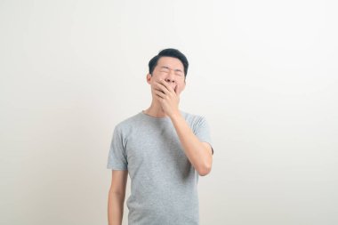 Esnemiş suratlı ve beyaz arka planda uykulu genç bir Asyalı.