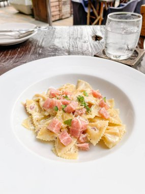 Beyaz tabakta jambonlu carbonara farfelle makarnası.