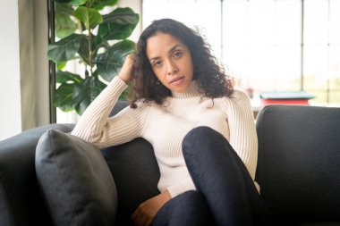 Latin bir kadın evde kanepesinde yalnız başına oturuyor.