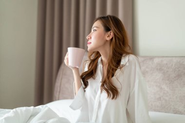 Portre güzel Asyalı kadın uyanır ve elinde kahve fincanı ya da kupayla sabah uyanır.