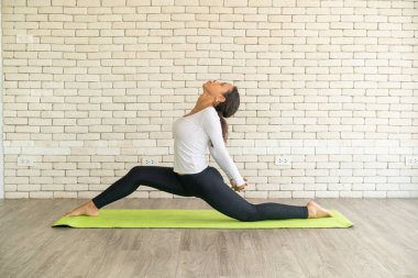 Latin kadın beyaz tuğlalı minder üzerinde yoga yapıyor.