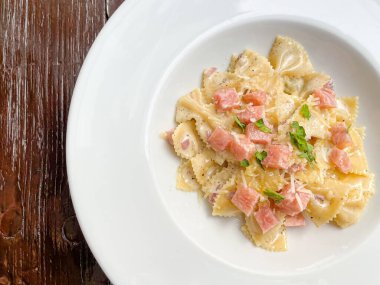 Beyaz tabakta jambonlu carbonara farfelle makarnası.