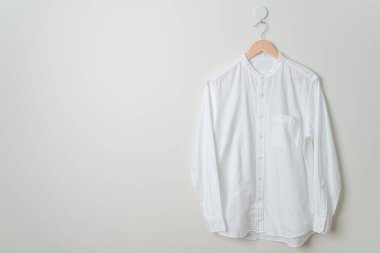 Duvarında ahşap askı olan beyaz gömlek asılı.