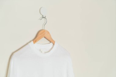 white t-shirt hanging with wood hanger on wall