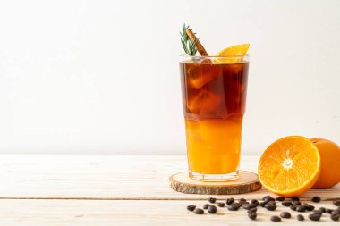 Bir bardak buzlu americano sade kahve ve ahşap arka planda biberiye ve tarçınla süslenmiş portakal ve limon suyu.