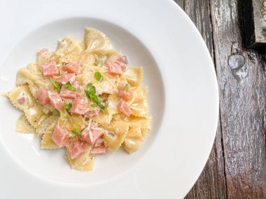 Beyaz tabakta jambonlu carbonara farfelle makarnası.