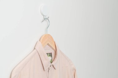 Duvarında ahşap askı olan bej bir gömlek asıyor.