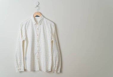 Duvarında ahşap askı olan bej bir gömlek asıyor.