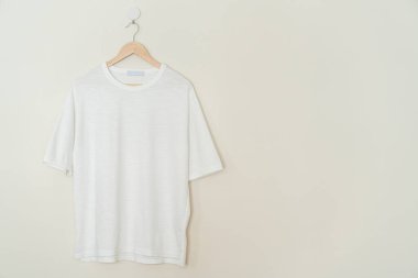 white t-shirt hanging with wood hanger on wall