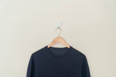 navy t-shirt hanging with wood hanger on wall