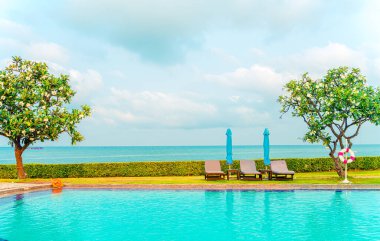 Sandalye havuzu ve şemsiyeyle okyanus arka planında yüzme havuzu